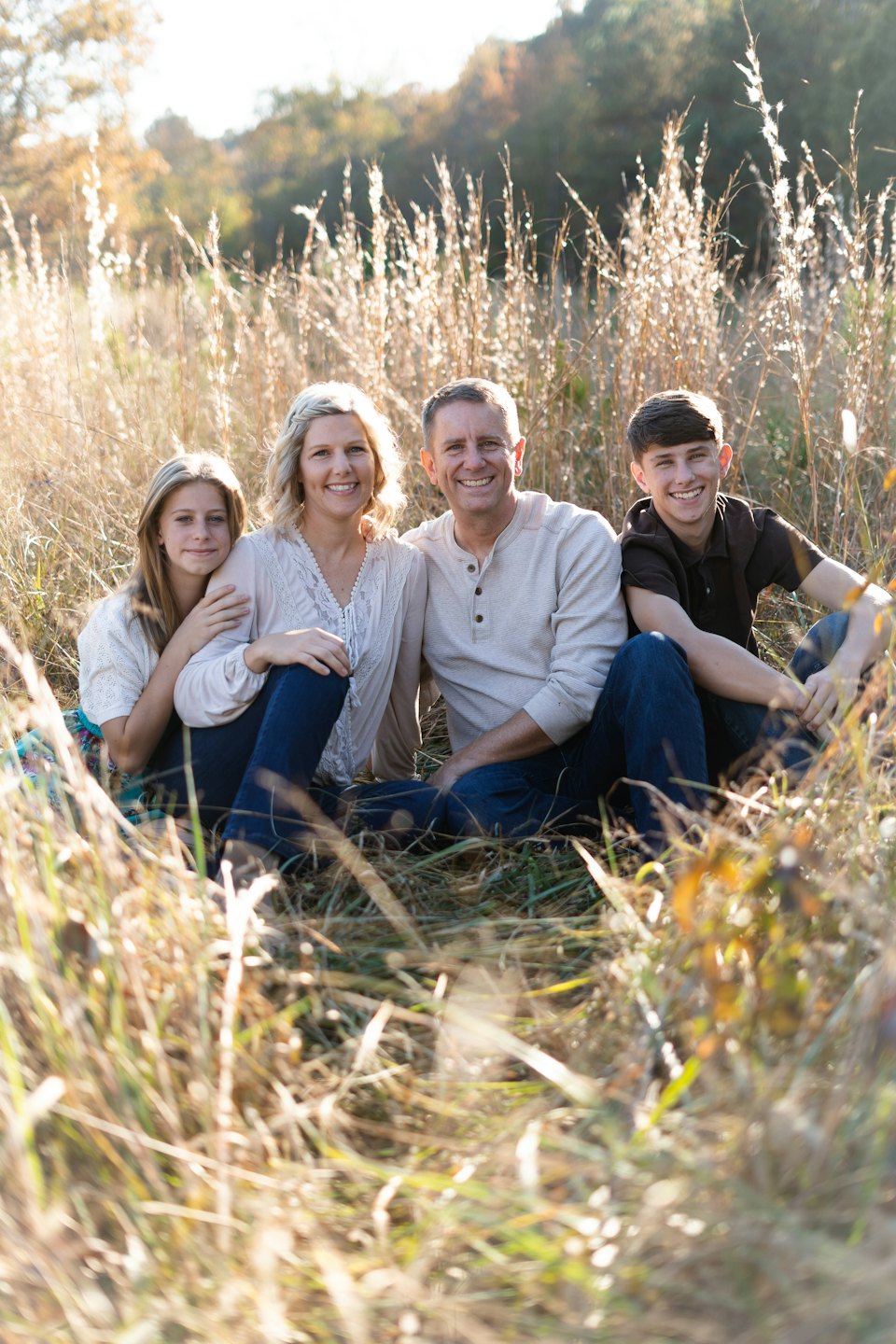 Family of four sitting together in tall dry grass.